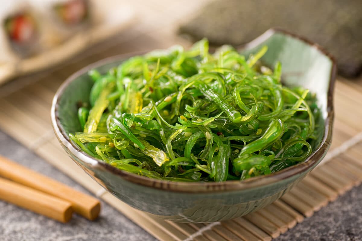 A bowl of fresh limu seaweed salad — bright green ogo strands dressed with sesame seeds and chopsticks resting alongside